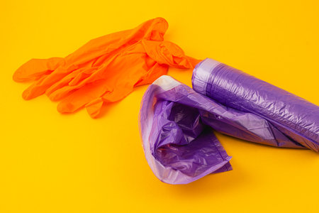 Bright orange gloves rest on vibrant yellow surface alongside crumpled purple plastic wrap,...