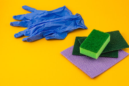 Colorful cleaning supplies including sponges and gloves are arranged neatly on a vibrant yellow surface, highlighting their utility for various cleaning tasks.の写真素材
