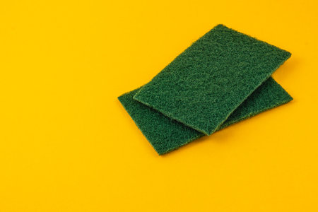 Two green cleaning pads are neatly stacked on a vibrant yellow background, perfect for household cleaning tasks and maintaining kitchen surfaces.の写真素材