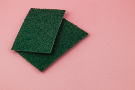 Two green cleaning pads are laid out on a light pink surface, highlighting tools commonly used for household cleaning tasks in kitchens.の写真素材
