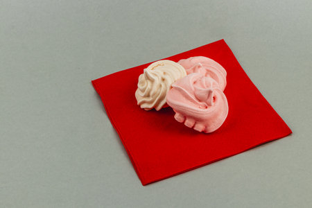 Delicate meringues in white and pink colors rest on a bright red napkin. The treat offers a playful contrast, perfect for a dessert table or celebration.の写真素材