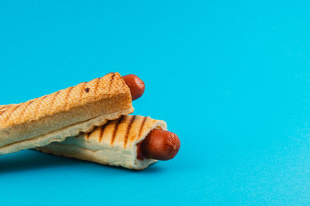 Grilled hot dogs nestled in crispy bread are beautifully arranged against a bright blue background, showcasing a fun and appetizing culinary creation.の写真素材