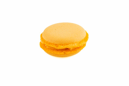 An orange macaron sits on a white surface, showcasing its smooth texture and vibrant color, ready to be enjoyed as a sweet treat.の写真素材