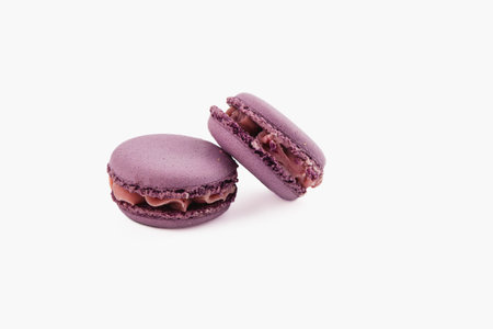 Two vibrant purple macarons filled with smooth chocolate cream are arranged together. These delicate treats showcase a perfect texture and delightful color.の写真素材