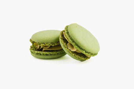 Two green macarons sit side by side, featuring a creamy nut filling. The bright color and smooth texture showcase the delicate pastry work behind them.の写真素材