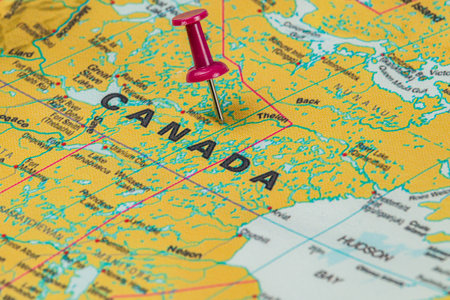 A detailed map of Canada highlighting various geographical features, with a bright red pushpin indicating a specific point of interest in the country.の写真素材