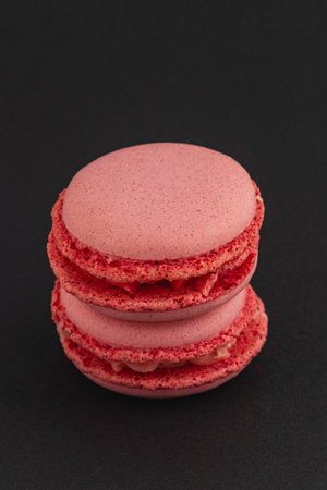 Two red macarons are stacked neatly against a dark background, showcasing their smooth exterior and delicate filling, creating a tempting dessert display.の写真素材