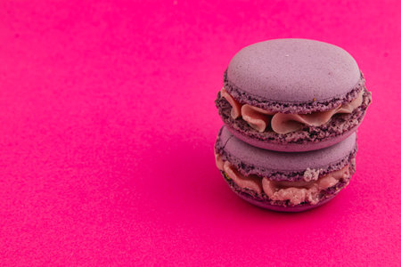Two stacked purple macarons filled with creamy filling sit against a bright pink backdrop, showcasing their rich color and enticing texture.の写真素材