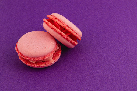 Two pink macarons sit on a bright purple background, showcasing their delicate texture and filling. These treats offer a striking contrast to the vivid color beneath.の写真素材