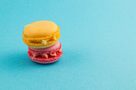 Two vibrant macarons, one yellow and one pink, are stacked neatly against a bright blue background, showcasing their delightful textures and colors.の写真素材