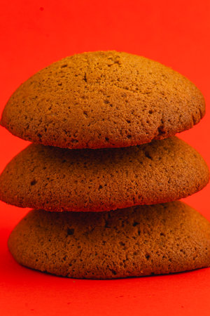Three perfectly baked ginger cookies are stacked together, showcasing their inviting texture and warm brown color against a bright red backdrop, creating an appetizing look.の写真素材
