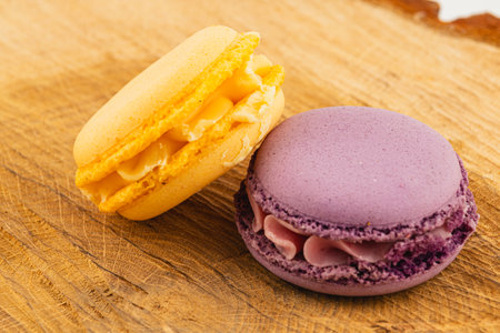Two vibrant macaron pastries are beautifully arranged on a rustic wooden board, showcasing their delicate textures and playful colors, perfect for dessert lovers.の写真素材