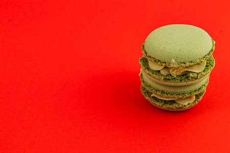 Three green macarons filled with cream are stacked neatly against a bright red background, showcasing their smooth texture and appealing colors.の写真素材