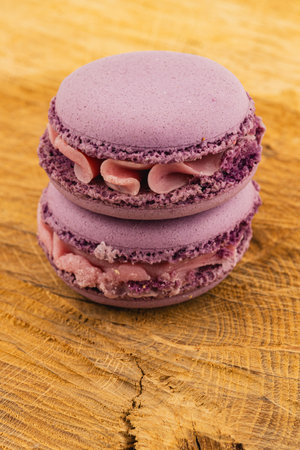Two lavender macarons with creamy filling sit on a textured wooden surface, showcasing their delicate color and elegant appearance, perfect for dessert lovers.の写真素材