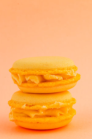 Two yellow macarons are stacked together against a soft pastel background. The delicate cookies have a creamy filling and showcase a vibrant color.の写真素材