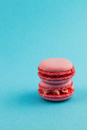 Three pink macarons with light cream filling are stacked on top of each other, set against a bright blue backdrop, creating a visually appealing dessert display.の写真素材