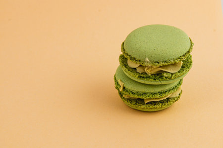 Three vibrant green macarons are stacked atop each other against a soft orange backdrop, highlighting their smooth texture and elegance.の写真素材