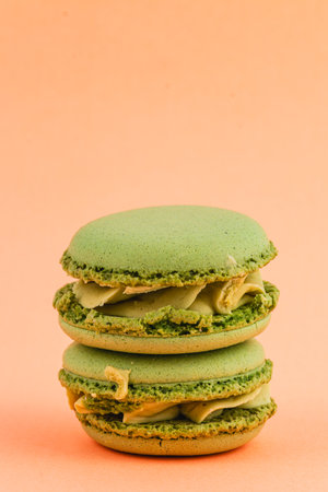 Two scrumptious green macarons are stacked together, showcasing creamy filling, set against a warm peach background, highlighting their appealing colors and textures.の写真素材