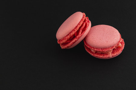 Delicate pink macarons sit beautifully on a sleek black surface, showcasing a smooth texture. Their vibrant color adds a touch of elegance to any dessert arrangement.の写真素材