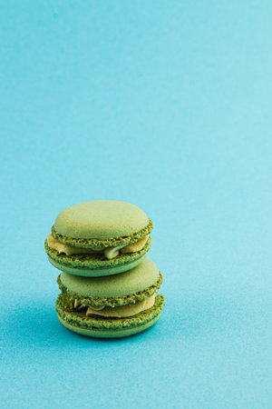 Three green macarons filled with cream are stacked against a bright blue backdrop, showcasing their texture and color. A delightful treat for dessert lovers.の写真素材