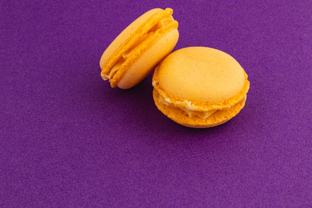 Two yellow macarons are placed on a rich purple backdrop, showcasing their smooth texture and creamy filling, creating an enticing visual treat.の写真素材