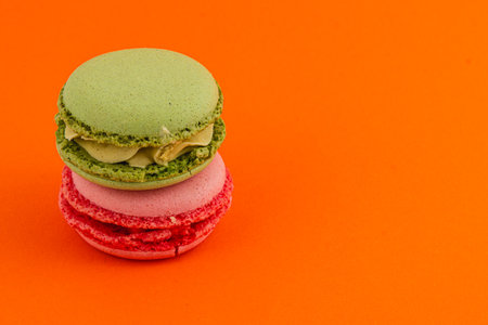 Two macarons are stacked, one green and one pink, creating a vibrant visual. The bright orange background highlights their colors and texture beautifully.の写真素材