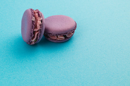 Two delicate purple macarons with a smooth chocolate filling rest on a bright blue surface, showcasing their elegant design and inviting appearance.の写真素材