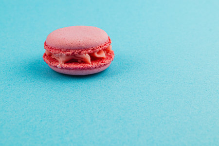 A single pink macaroon sits elegantly on a bright blue surface. The treat features a smooth cream filling and has a light, airy texture, showcasing its sweet appeal.の写真素材