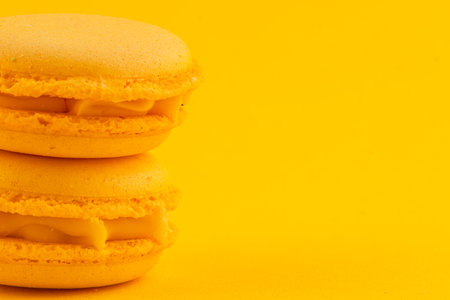 Two vibrant yellow macarons lie stacked against a cheerful yellow backdrop, showcasing their smooth texture and creamy filling, perfect for a dessert treat.の写真素材