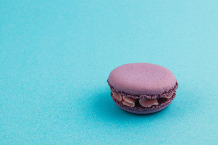 A single purple macaron sits on a vibrant blue surface, highlighting its delicate texture and filling. Perfect for anyone who enjoys sweet treats and pastries.の写真素材