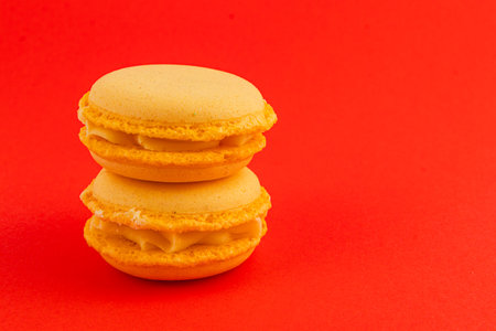 Two yellow macarons filled with cream are stacked on top of each other against a bright red background, showcasing their smooth texture and vibrant color.の写真素材