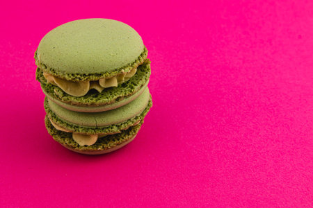 Three green macarons filled with a creamy filling are neatly stacked on a bright pink surface, highlighting their texture and color contrast.の写真素材