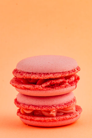 Two stacked pink macarons with a smooth filling are displayed on a bright orange background, showcasing their delicate texture and inviting color.の写真素材