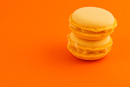 Two orange macarons with a creamy filling are stacked on a bright orange background, highlighting their texture and color perfectly.の写真素材