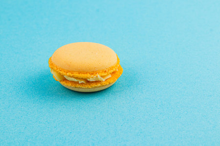 A single yellow macaron rests on a vibrant blue surface, showcasing its smooth texture and cream filling, creating a visually appealing treat.の写真素材
