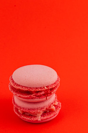 Two pink macarons are stacked on top of each other against a vibrant red background, highlighting their textured shell and creamy filling.の写真素材