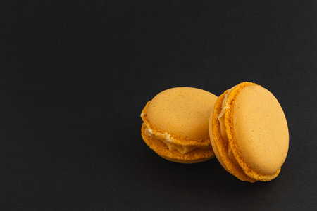 Two golden yellow macarons sit elegantly on a black surface, showcasing their delicate texture and creamy filling that invites indulgence.の写真素材