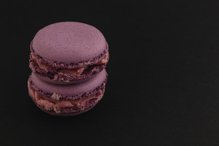 Two beautifully crafted purple macarons are stacked on a dark background, showcasing their smooth texture and creamy filling, perfect for dessert lovers.の写真素材