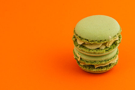 Delicious green macarons filled with creamy filling are stacked against a vibrant orange backdrop, creating a striking and appetizing visual contrast.の写真素材