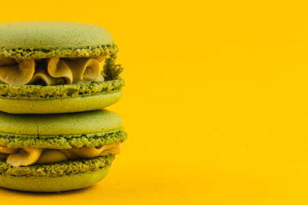 Two green macarons filled with creamy frosting are stacked against a vibrant yellow backdrop, showcasing a delightful pastry treat perfect for dessert lovers.の写真素材