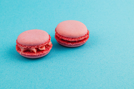 Two raspberry macarons sit invitingly on a bright turquoise surface, showcasing their smooth texture and vibrant color.の写真素材