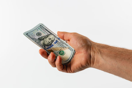 A hand extends forward, firmly grasping a one hundred dollar bill. The bill is clearly visible...