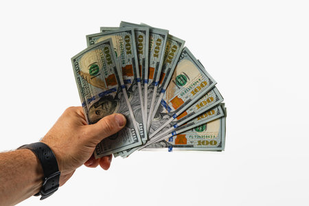 A hand is displaying a fan of hundred dollar bills in front of a neutral gray background, showcasing...