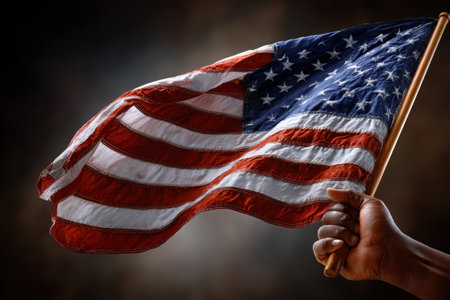 A close-up captures a hand tightly gripping a flagpole while an American flag flutters vigorously in the wind, symbolizing patriotism and resilience.の素材