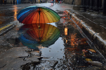 A vibrant rainbow umbrella stands against the backdrop of a wet city street. Puddles reflect colorful hues, creating a serene atmosphere during rainfall.の素材