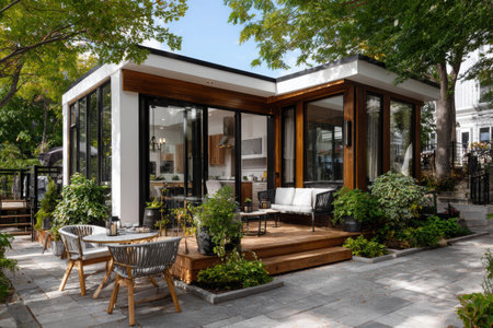 A tiny house showcases modern Scandinavian design with white and wood tones. It features a patio adorned with outdoor chairs, surrounded by lush greenery and clean pavement.の素材
