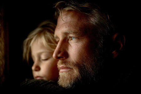 A tired father gazes thoughtfully into the distance while holding his sleeping child on his shoulder. The soft ambient light enhances the depth of their bond and emotional fatigue.の素材