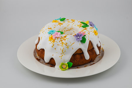 A round cake featuring white icing draped over the top, adorned with vibrant flowers and decorative...