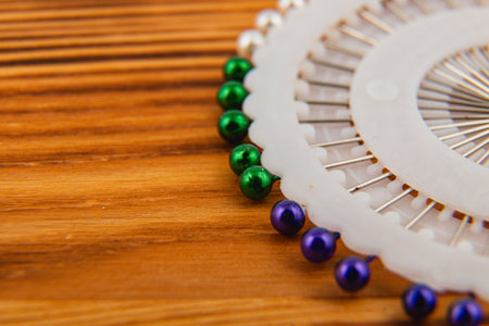 Close-up of beading tools with green and purple beads on a wooden surface showcases crafting...