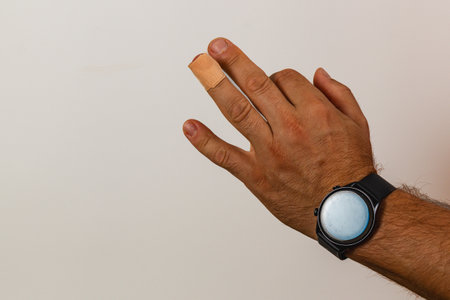 A hand with a bandaged finger is positioned against a plain background. The person's wrist features a round watch, highlighting a casual style and minor injury.の写真素材